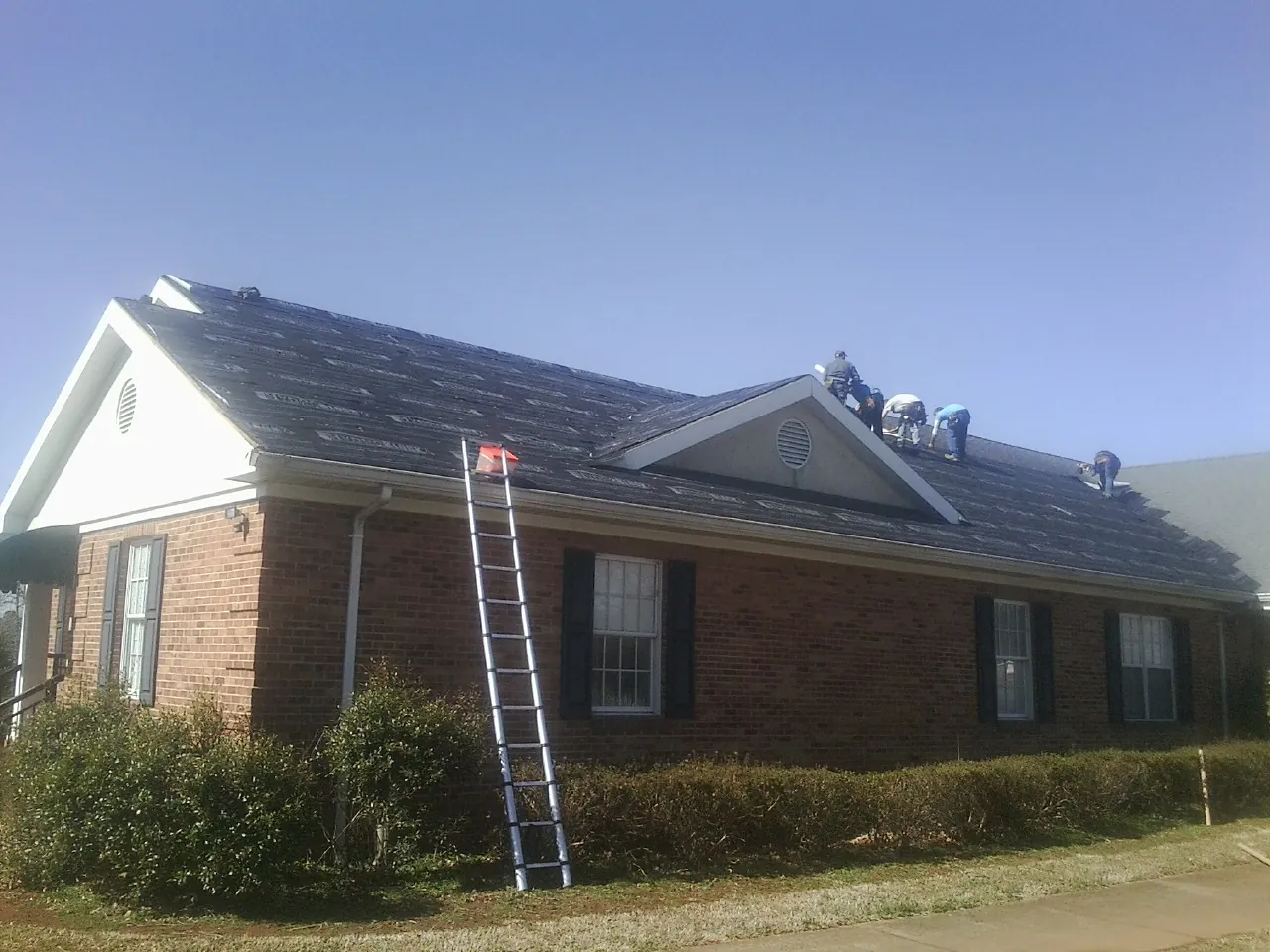 Crew tearing shingles off a brick ranch roof with a ladder set — Metal Roof Repair work by our crew in Mahwah