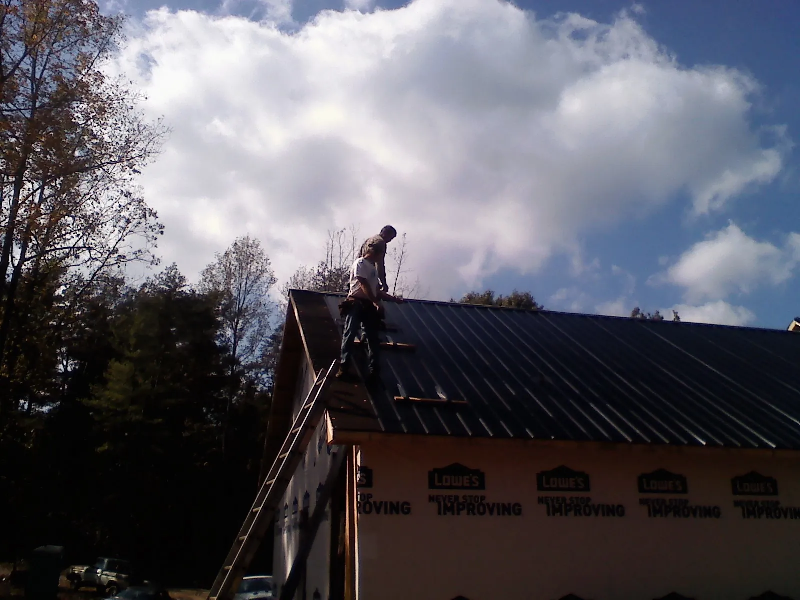 Roofer fastening dark metal panels high against a cloudy sky, from a Roof Inspection job in Mahwah