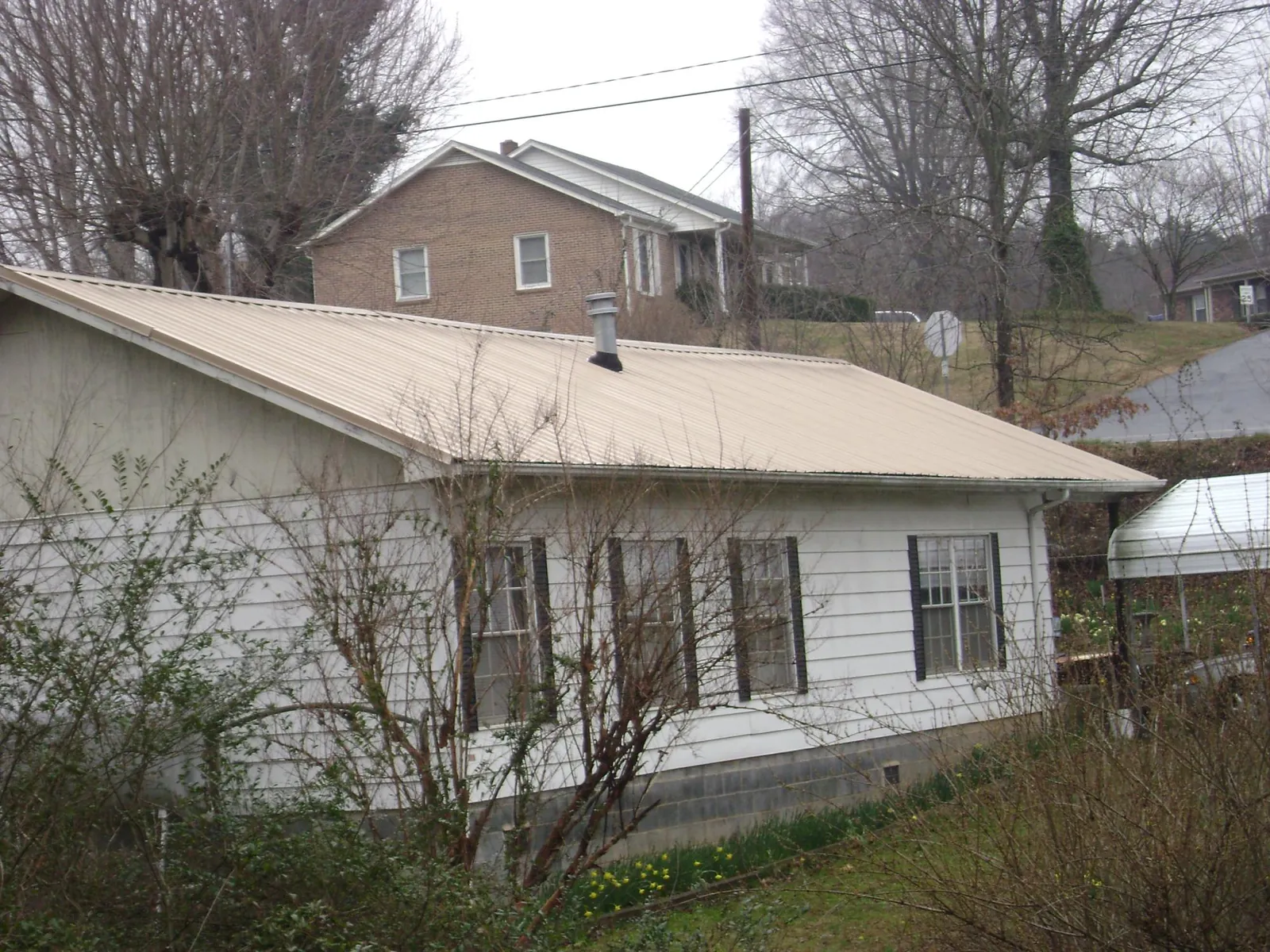 Tan metal roof on a white sided house set into a hillside — Commercial Roofing by Roofing Brothers in Mahwah
